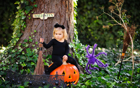 Маленькая девочка сидит на тыкве в лесу в костюме на Хэллоуин 