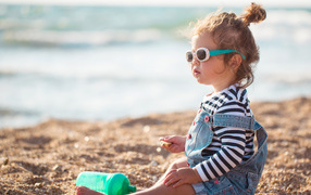 Маленькая девочка сидит на песке на пляже