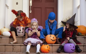 Маленькие дети в костюмах на Хэллоуин сидят на ступеньках со сладостями