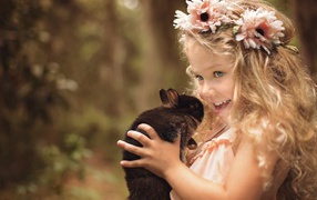 Маленькая улыбающаяся девочка с венком на голове держит кролика