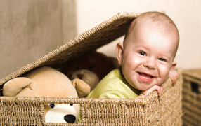 Улыбающийся забавный малыш в плетеной корзине с игрушками