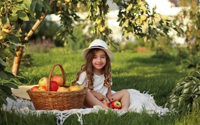 Улыбающаяся девочка сидит на зеленой траве с яблоками