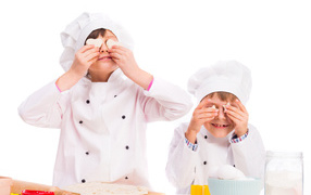 Два маленьких мальчика в костюмах повара на кухне делают печенье