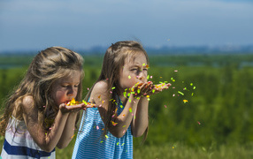 Две маленькие девочки сдувают конфетти  с рук