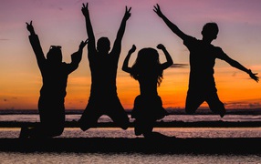 Silhouettes of young people jumping by the sea