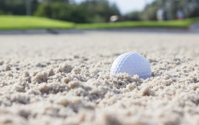 White golf ball lying on the sand