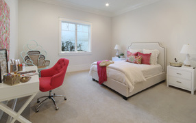 Спальня в светлых тонах с кроватью и столом с красным креслом