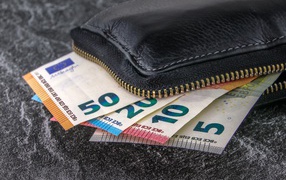 Euro bills lie in a black leather wallet