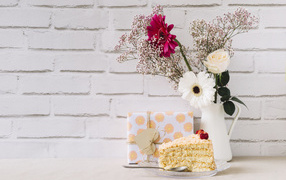 A piece of cake, a gift and a bouquet on a table on a wall background
