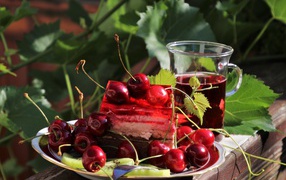 A piece of cake with cherries on a table with a cup of tea