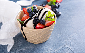 Шарики мороженого в стакане на столе с клубникой и ягодами черники
