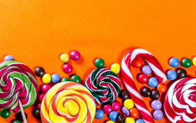 Разноцветные шоколадные и карамельные конфеты на оранжевом фоне