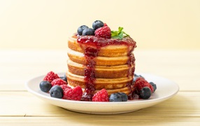 Rosy pancakes with jam and blueberries and raspberries on a plate