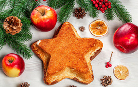 Пирог в форме звезды на столе с яблоками и еловыми ветками 