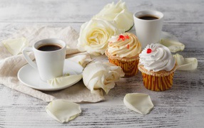 Две чашки кофе на столе с белыми розами и кексами