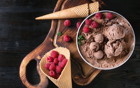 Вафельный рожок с шоколадным мороженым и ягодами малины на столе