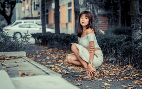 Красивая девушка азиатка в белом платье сидит в осеннем парке 