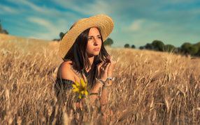 Красивая девушка в шляпе сидит на поле с пшеницей