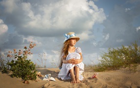 Красивая девочка в белом платье сидит на песку