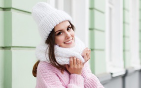 Красивая улыбающаяся девушка в розовом свитере и теплой шапке 