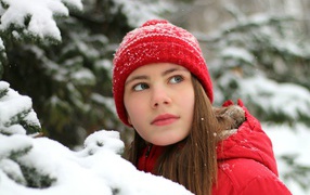 Cute little girl in a red hat by a snowy spruce