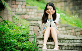 Мечтательная девушка азиатка сидит на ступеньках 