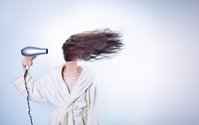 Девушка сушит волосы феном на сером фоне