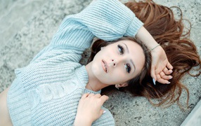 Длинноволосая девушка в голубом свитере лежит на земле 