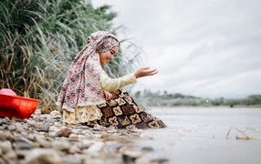 Улыбающаяся девушка азиатка сидит у воды
