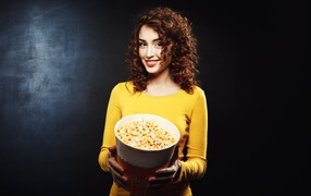 Smiling girl with popcorn in hands on black background
