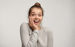 Surprised girl with hand near face on gray background