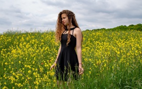 Молодая девушка в черном платье на поле с желтыми цветами