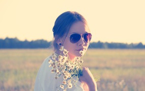 Молодая девушка в солнечных очках с букетом ромашек на поле