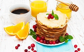 Тонкие румяные блинчики на столе с ягодами клюквы, апельсинами, медом и кофе