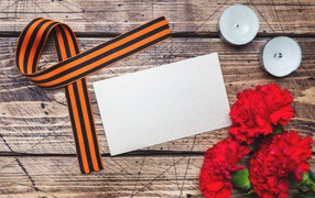Red carnations, St. George ribbon and candles on the table, template for greeting card on May 9 Victory Day