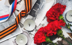 Three carnations, candles and ribbons on old photos on May 9 Victory Day