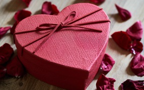 Big red heart-shaped box on a table with rose petals