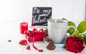 White cup with sweets and a red rose on the table as a gift for February 14