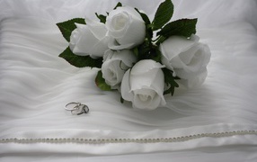 White boutonnieres with rings on a white bedspread