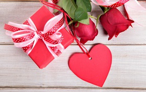 Красные розы с подарком и красным сердцем на деревянном столе