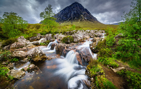 Fast water in the river against the backdrop of a high mountain under a stormy sky