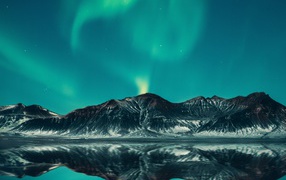 Green aurora borealis in the sky above the mountains by the lake