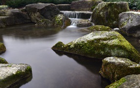 Water flows down stones into a pond with large moss-covered stones