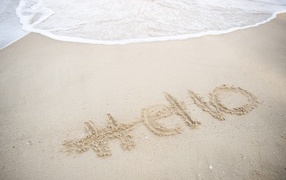 Hello lettering on wet sand by the sea in summer