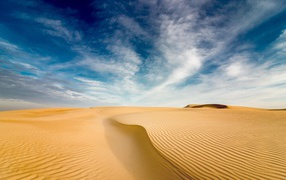 Sand dune under a blue sky with white clouds