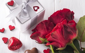 Букет красных роз на столе с конфетами и подарком