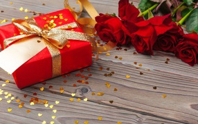 Bouquet of red roses with a big gift on the table