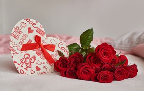 Bouquet of red roses with a heart-shaped box on the bed