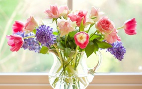 Bouquet of roses, tulips and hyacinths in a glass vase by the window