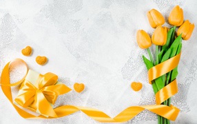 Bouquet of yellow tulips with a ribbon and a gift on a gray background